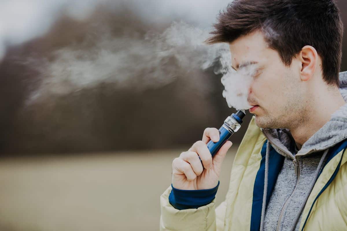 A man smoking an electronic cigarette in a field, pondering how long does a delta 8 cart last.