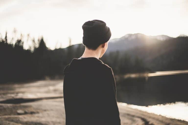 a man wearing a black beanie is standing by a lake.