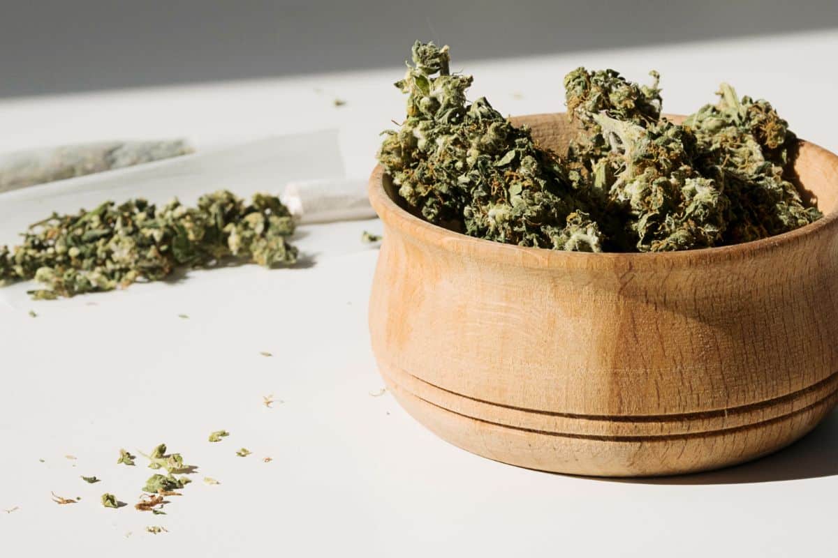Grape jelly strain marijuana in a wooden bowl on a white table.