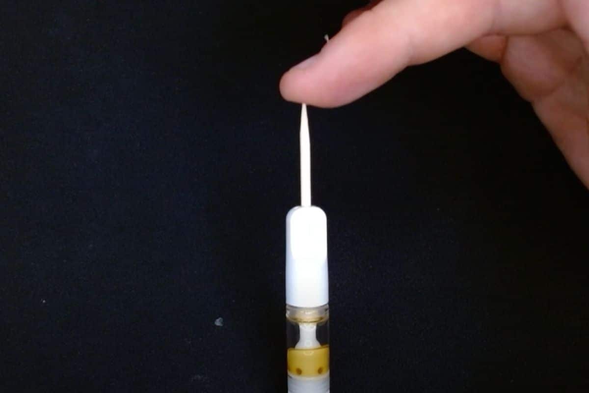 A guy unclogging his vape cart with the help of a toothpick.