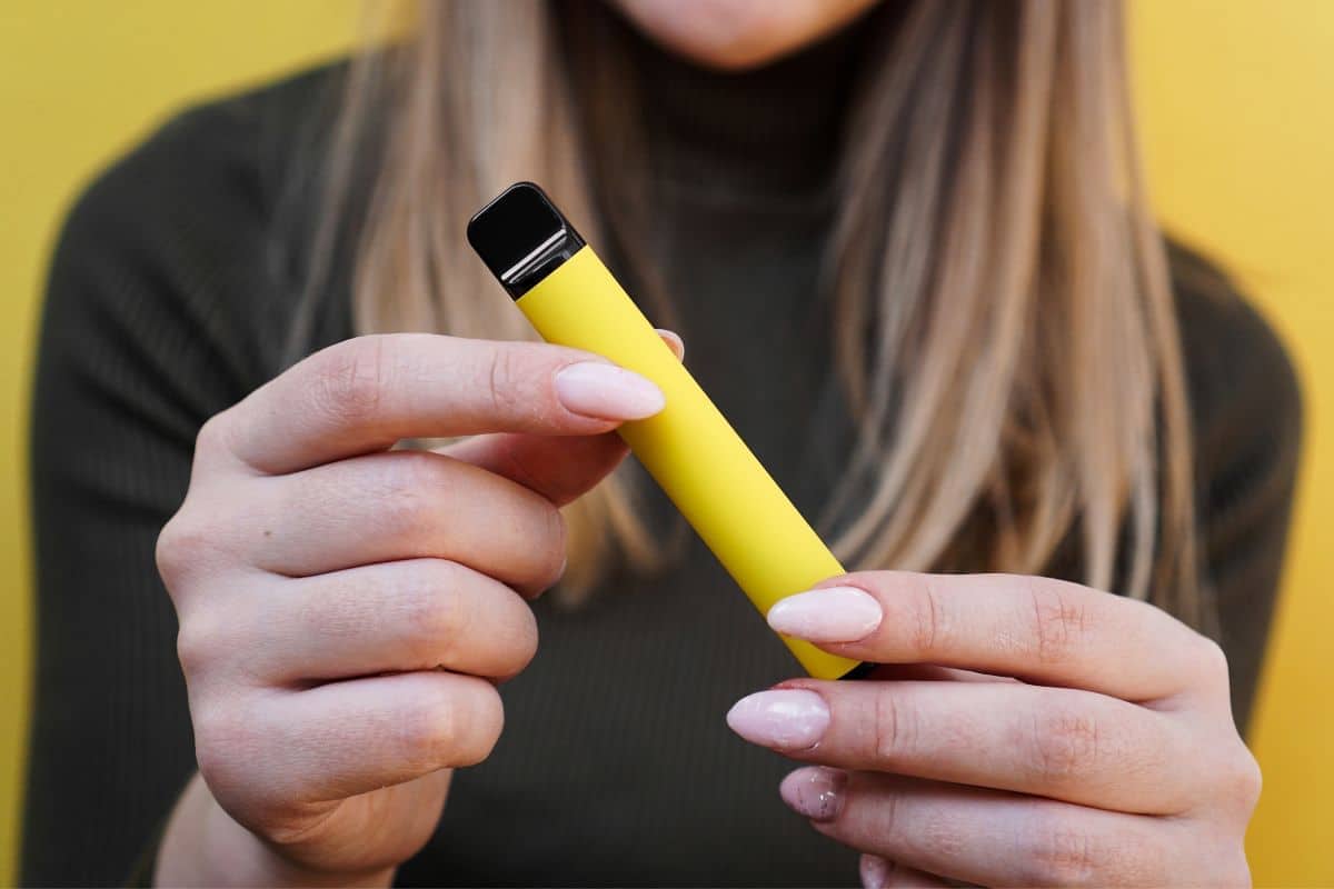 A woman gracefully holding a yellow electronic cigarette, demonstrating how to use a disposable vape pen to get dazed.