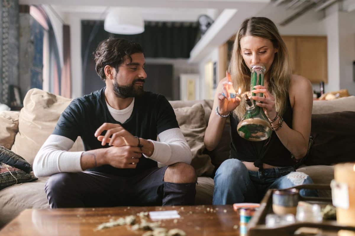 A man and woman **dabbing** marijuana on a couch.