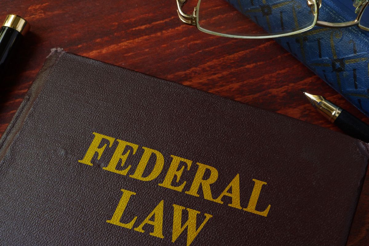 A fedral law book kept on the table containing law regarding mails accompanied by a pen and eyeglasses.