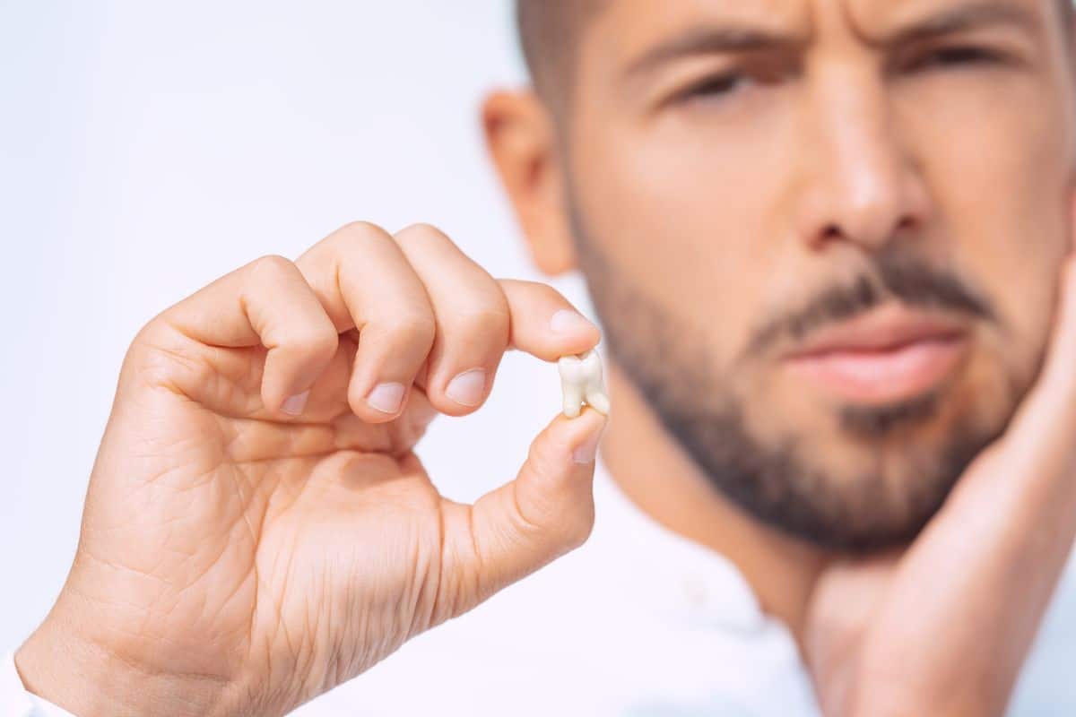 A man is holding a small pill in his hand, wondering when he can vape after wisdom teeth removal.