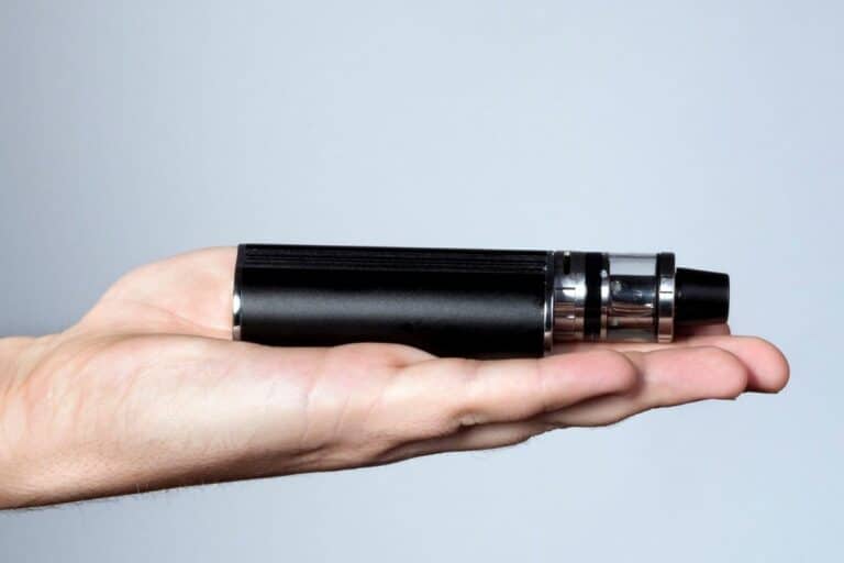 A hand holding a black electronic cigarette, which keeps hitting after I stop, against a grey background.