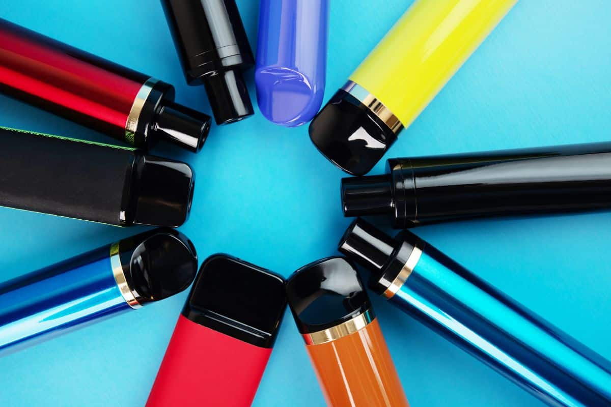 Colorful assortment of disposable vape markers arranged in a starburst pattern on a blue background.