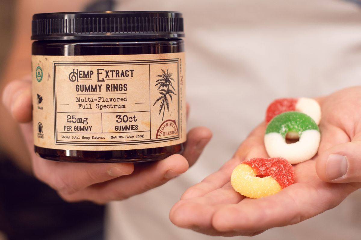 A person holding jar of cbd gummies and some gummies in his left hand