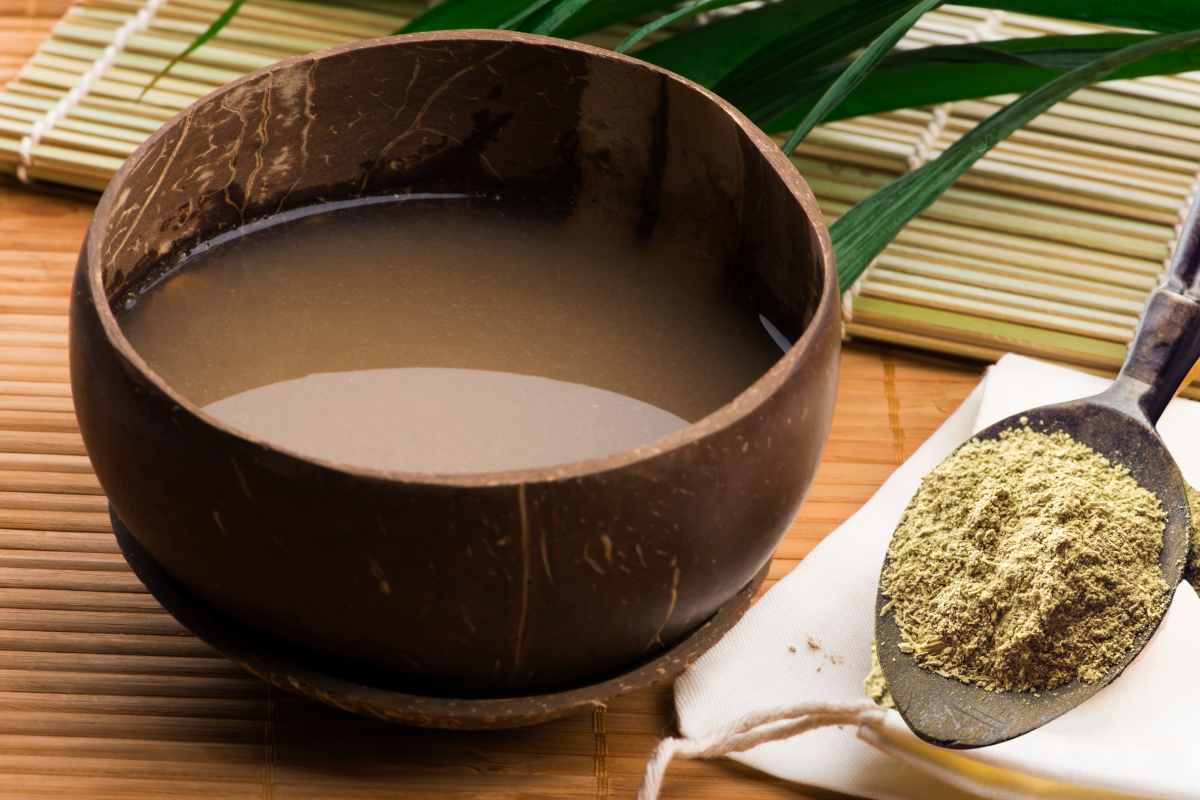 A bowl of kava with a spoonful of kratom powder placed beside it